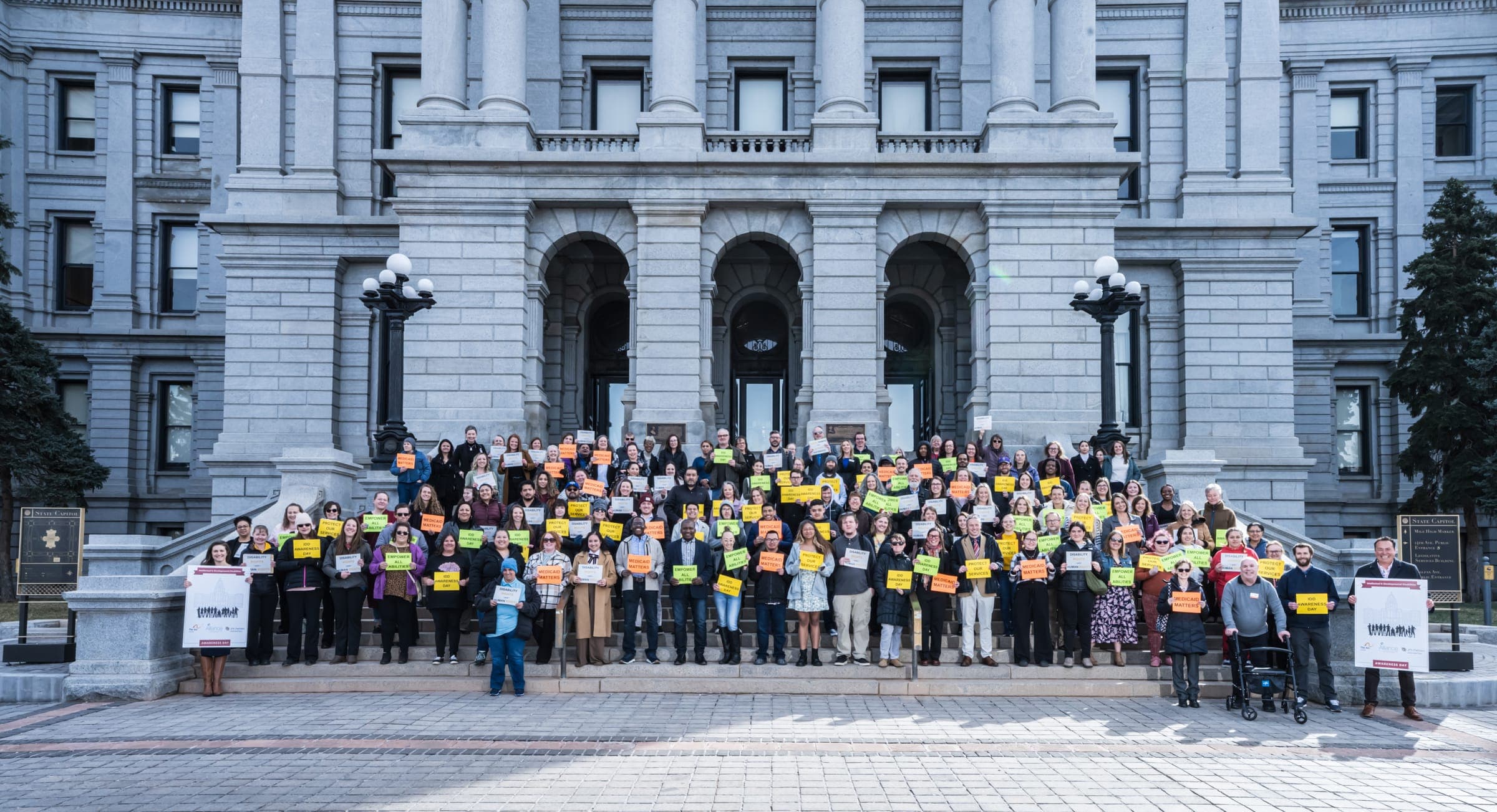 About 150 advocates holding signs such as Medicaid Matters and Protect Our Services on the steps of the Colorado State Capitol for IDD Awareness Day