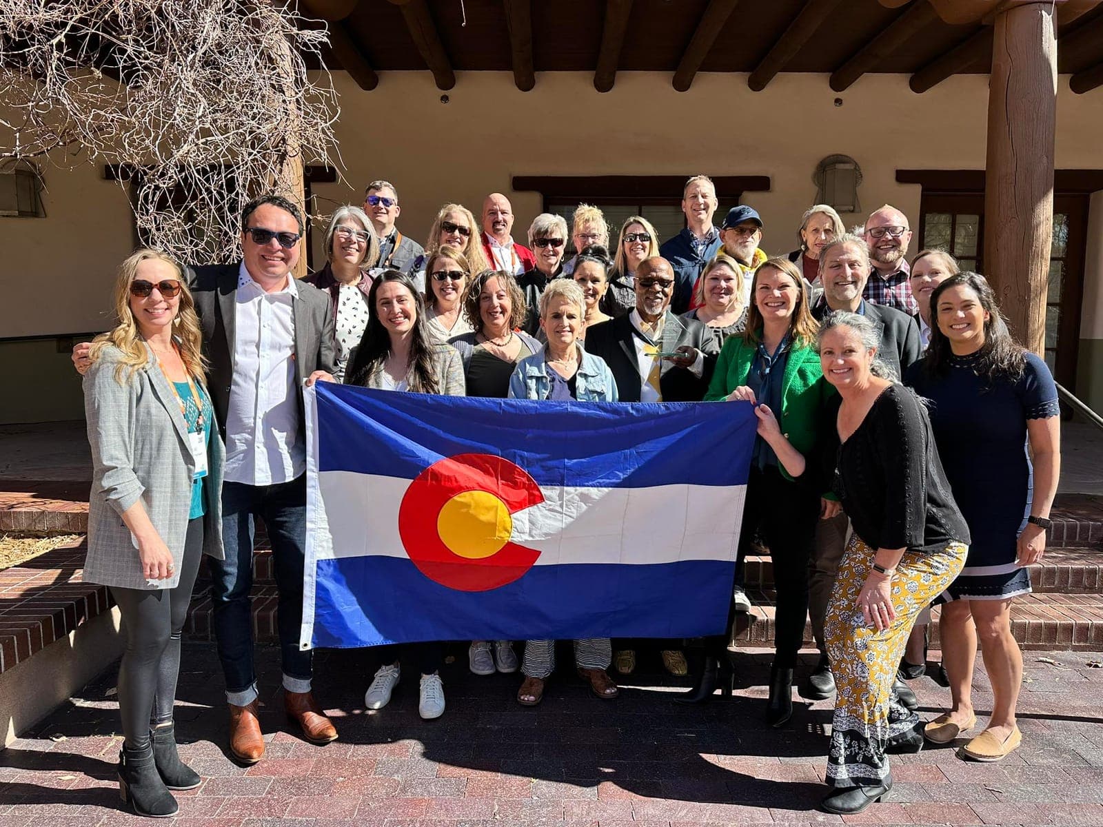 A group of people holding the Colorado Flag and smiling